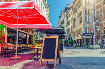 Street restaurant with tables and chairs on narrow street, road with paving stone, old buildings in Antwerp historical city center, street cafe in old town Antwerpen, Belgium