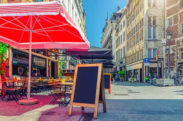 Plexiglas foto achterwand Street restaurant with tables and chairs on narrow street, road with paving stone, old buildings in Antwerp historical city center, street cafe in old town Antwerpen, Belgium © Aliaksandr