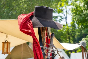Fotobehang A black felt hat and the hilt of a medieval sword in a military camp © ZenitX