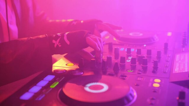 DJ plays music in a nightclub with multicolor effect and smoky room.