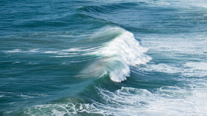 Sunlight catches the spray of a powerful, cresting ocean wave, highlighting the dynamic motion and...