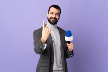 Adult reporter man with beard holding a microphone over isolated purple background doing coming gesture