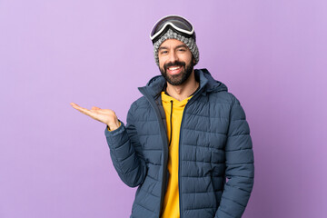 Skier man with snowboarding glasses over isolated purple background holding copyspace imaginary on the palm to insert an ad