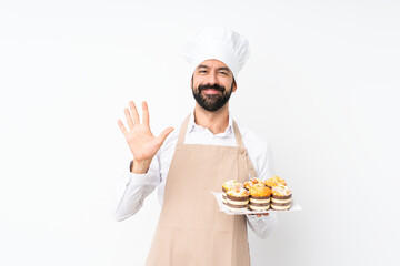 Young man holding muffin cake over isolated white background counting five with fingers