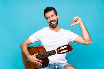 Young man with guitar over isolated blue background proud and self-satisfied