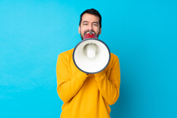 Young caucasian man over isolated blue background shouting through a megaphone