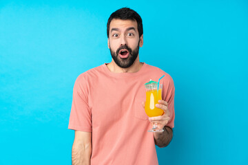 Young man over holding a cocktail over isolated blue background with surprise facial expression