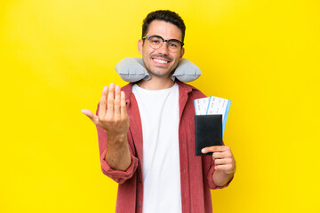 Young handsome man with Inflatable Travel Pillow over isolated yellow background inviting to come with hand. Happy that you came