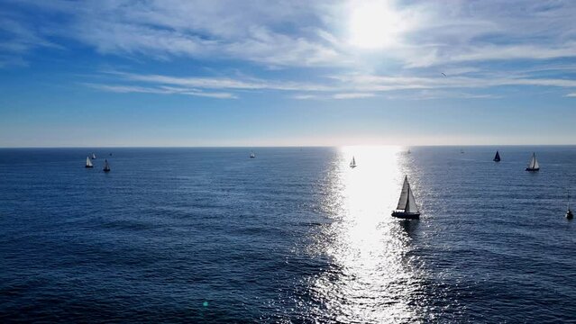 A small sailboat is navigating through the vast open ocean, surrounded by nothing but water. The sail flaps in the wind as the boat glides along the waves.