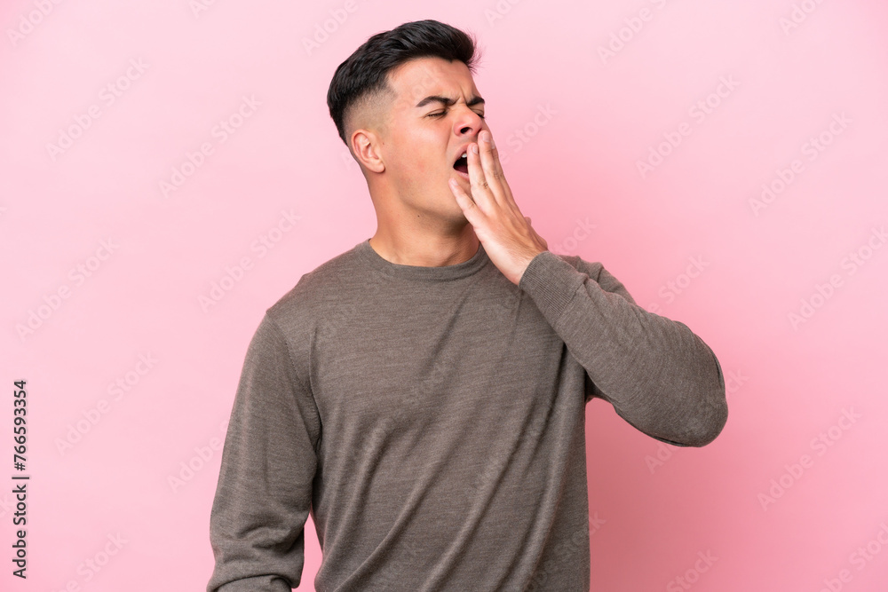 Poster Young caucasian handsome man isolated on pink background yawning and covering wide open mouth with hand