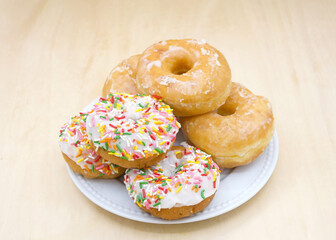 White porcelain plate with glazed and frosted cake donuts with sprinkles on a light wood table.