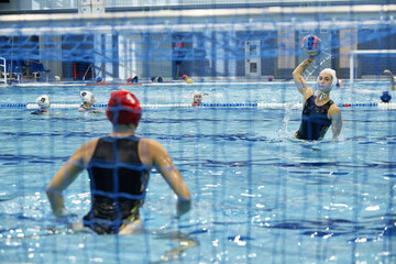 Focus on young sportswoman in swimwear throwing ball to gate of rival team during water polo game while standing in swimming pool