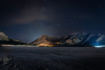Night sky over the edge of the Rockies and a frozen Lac Des Arcs