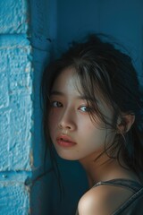 Fototapeta premium A young woman leaning against a blue wall. Suitable for lifestyle and fashion concepts