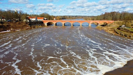 Large ancient bridge made of red brick on Venta River in the Latvian city of Kandava in spring of 2023