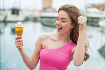 Young redhead woman with a cornet ice cream at outdoors celebrating a victory