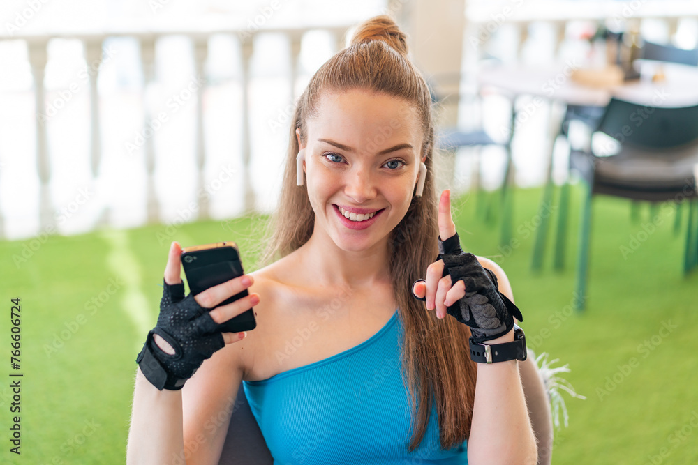 Poster Young pretty sport girl using mobile phone at outdoors pointing up a great idea