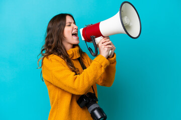 Young photographer woman isolated on blue background shouting through a megaphone