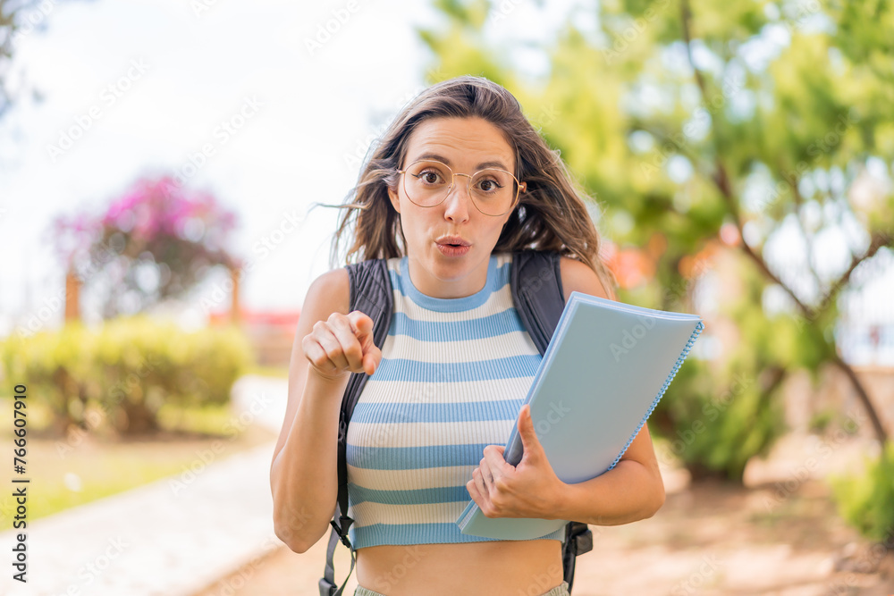 Wall mural Young pretty student woman at outdoors surprised and pointing front