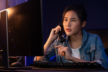 Obraz na płótnie Canvas Young beautiful Asian creative woman calling on phone desk to customer or coworker explaining creator project's high profit while searching market analysis on pc at neon office at night. Stratagem.