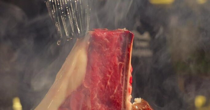 T-bone meat steak on barbecue charcoal grill, chef brushes steak with oil. Grilling BBQ meat. Smoke rising over juicy beef steak