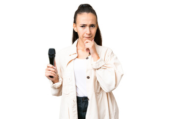 Young singer woman picking up a microphone over isolated chroma key background having doubts and...