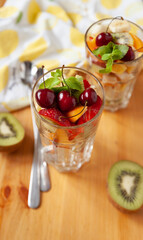 View from the top to large transparent glasses with chopped fruits and berries and long spoons on the table. Mandarin, kiwi, banana, strawberries, blueberries, cherries and mint leaves. Healthy snack. - 766620794