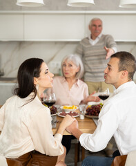 Young man and woman flirting sitting around table together with old family members who are watching...