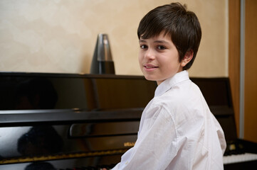 Close-up portrait of a multi ethnic teen boy, little pianist musician smiling looking at camera,...