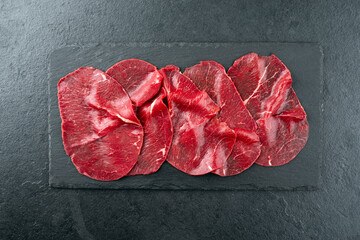 Traditionelle Carpaccio vom Rind serviert als Draufsicht auf einer schwarzen Design Platte mit...