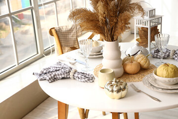 Autumn table setting with pampas grass and pumpkins in light kitchen near big window, closeup