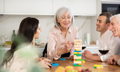 Elderly woman engrossed in playing jenga with husband, adult son and daughter-in-law during family...