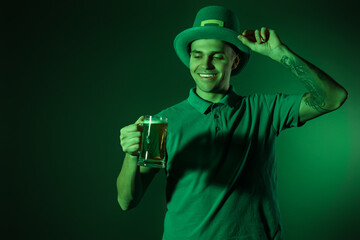 Happy young tattooed man with beer on dark green background. St. Patrick's Day