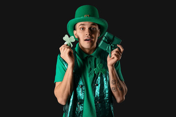 Surprised young man with clover and gift on dark background. St. Patrick's Day