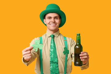Happy young man in leprechaun's hat, with beer and shamrock on yellow background. St. Patrick's Day