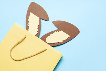 Shopping bag with paper Easter bunny ears on blue background