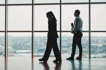 A man and a woman are standing in the office against the background of a large panoramic window....