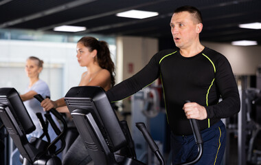 Middle-aged man in the gym is engaged in sports using an ellipsoid simulator. Healthy lifestyle and sport concept