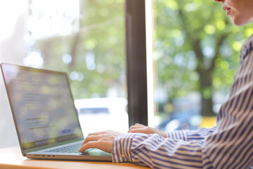 A woman works on a laptop at home or in an office near a window. Women's hands close-up, remote work, freelancer, study and complete tasks on the laptop.