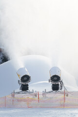 Schneekanonen beschneien die Piste mit Kunstschnee für Skifahrer und Snowboarder bei Frost im...