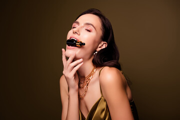 Photo of tempting gentle lovely woman biting jar with tinted moisturizer isolated on brown color...