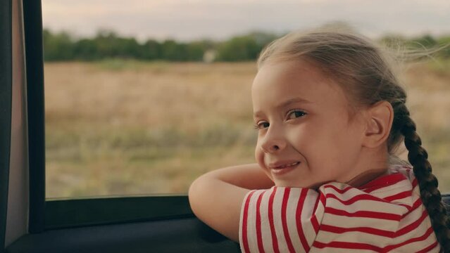 Child looks out of car window, enjoying trip. Happy family travels by car. Little girl kid enjoys family trip by car. Girl child looks out of car window. Child holiday emotion. Family vacation. Road