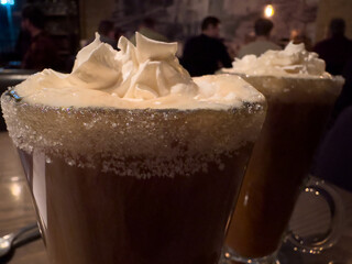 Two clear glass mugs of Irish coffee with whipped cream and a sugar rim. The thick white cream is floating on top of the hot coffee and strong whisky. The rim of the glass is covered with sugar.