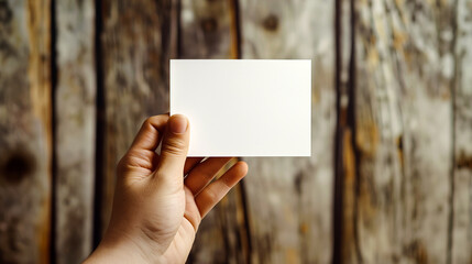 Close-up photo of a hand holding a white business card in front of a blurred wooden background Perfect for mockup designs - Generative AI