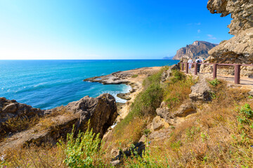 Scenic view of tourists on a walking path at the Arabian Sea and coastline of Mughsail beach, with the Dhofar mountains in view in Salalah, Oman.