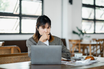 Businesswoman appears deep in thought while reviewing information on her laptop at a cafe, possibly...