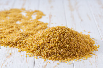 Pile of bulgur on a white wooden table. Heap of dry bulgur ion a white wooden table.
