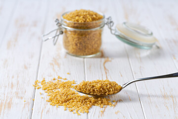 metal spoon with raw bulgur on a white wooden table.