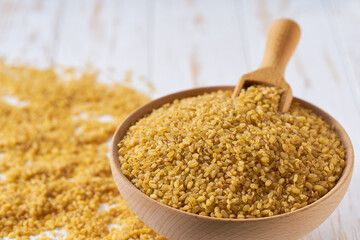 Organic dry bulgur are scattered in a wooden bowl close up.