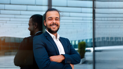Confidence successful businessman in suit with beard standing in front of office glass building lean on wall arm crossed looking at camera and smile. Hispanic modern business man portrait. Banner